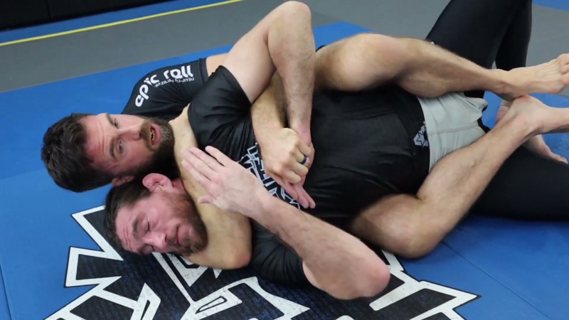 The attacker applies a rear naked choke from the back, with both hooks in and the choking arm around the neck.